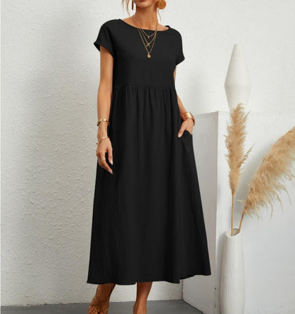 Frau in einem rosa fließenden Sommerkleid steht an einer weißen Wand